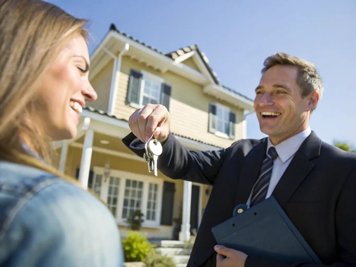 A real estate agent handing keys to a happy new homeowner in front of a newly purchased house.
